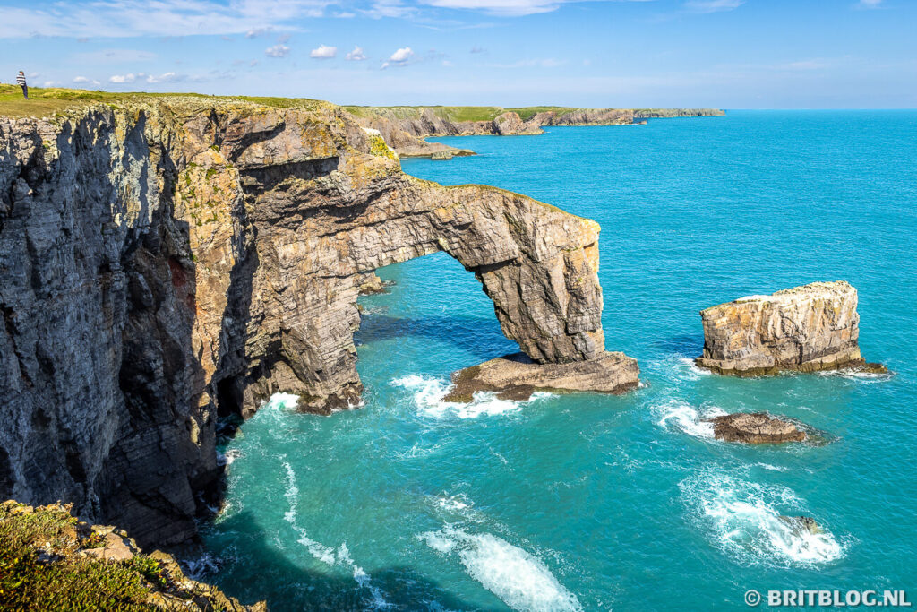 Natuurlijke kalkstenen brug Green Bridge of Wales met gras en vegetatie op de top, gelegen aan de ruige zuidkust van Pembrokeshire