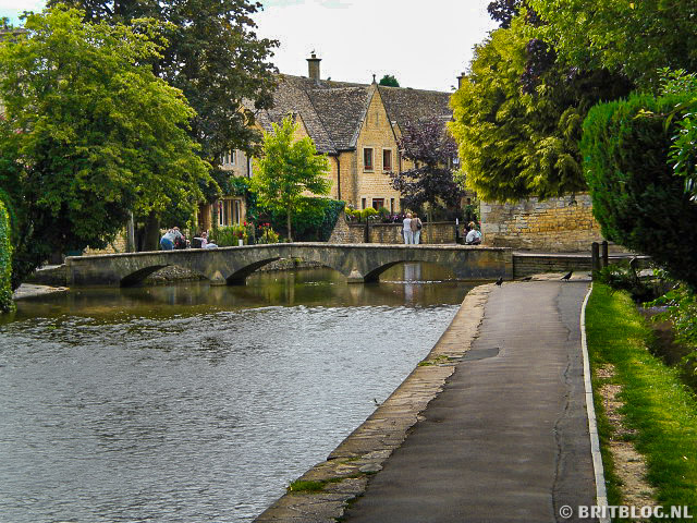 Stenen voetgangersbrug over de rivier Windrush in Bourton-on-the-Water, Cotswolds, omringd door bomen en cottages