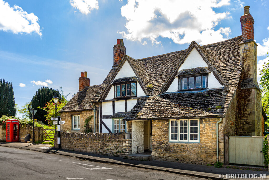 Traditionele cottage met vakwerk en stenen dak in Lacock, Cotswolds, met iconische rode telefooncel op de hoek van de straat