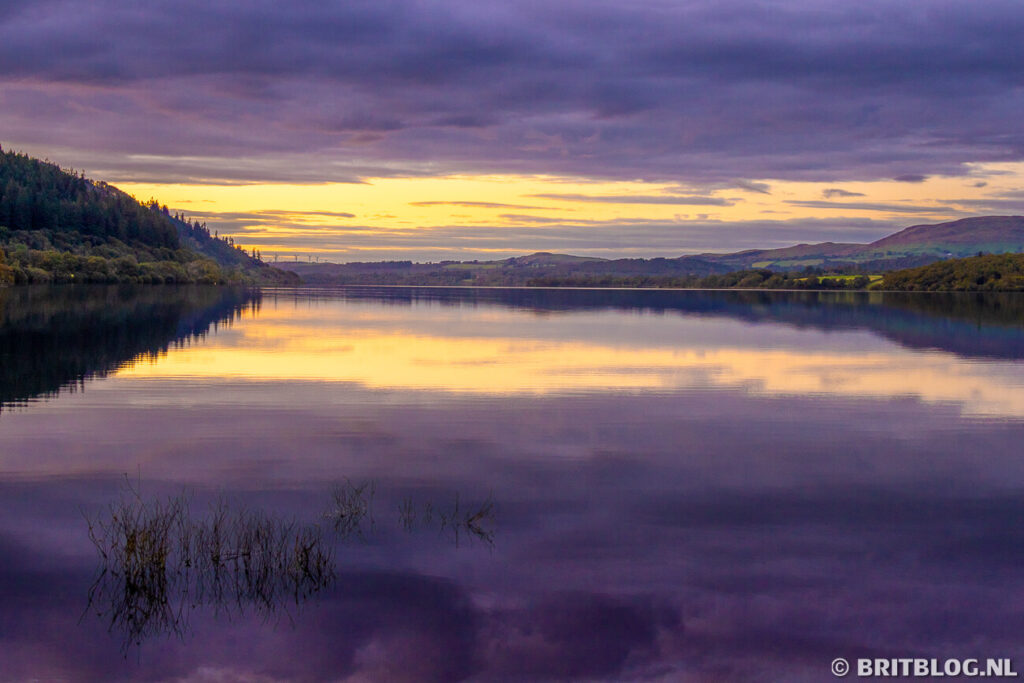 Zonsondergang boven Bassenthwaite Lake in het Lake District, met paarse wolken en weerspiegeling van de hemel in het kalme water.