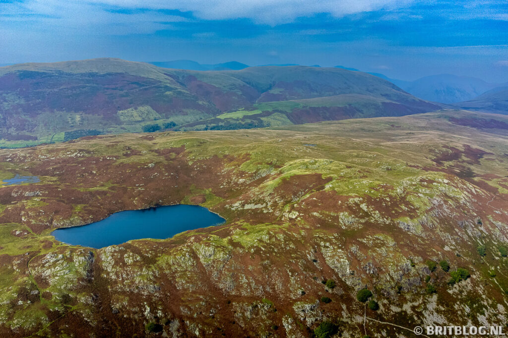 Luchtfoto van Blae Tarn bij Boot in het Lake District, met helderblauw water tussen groene en bruine heuvels.