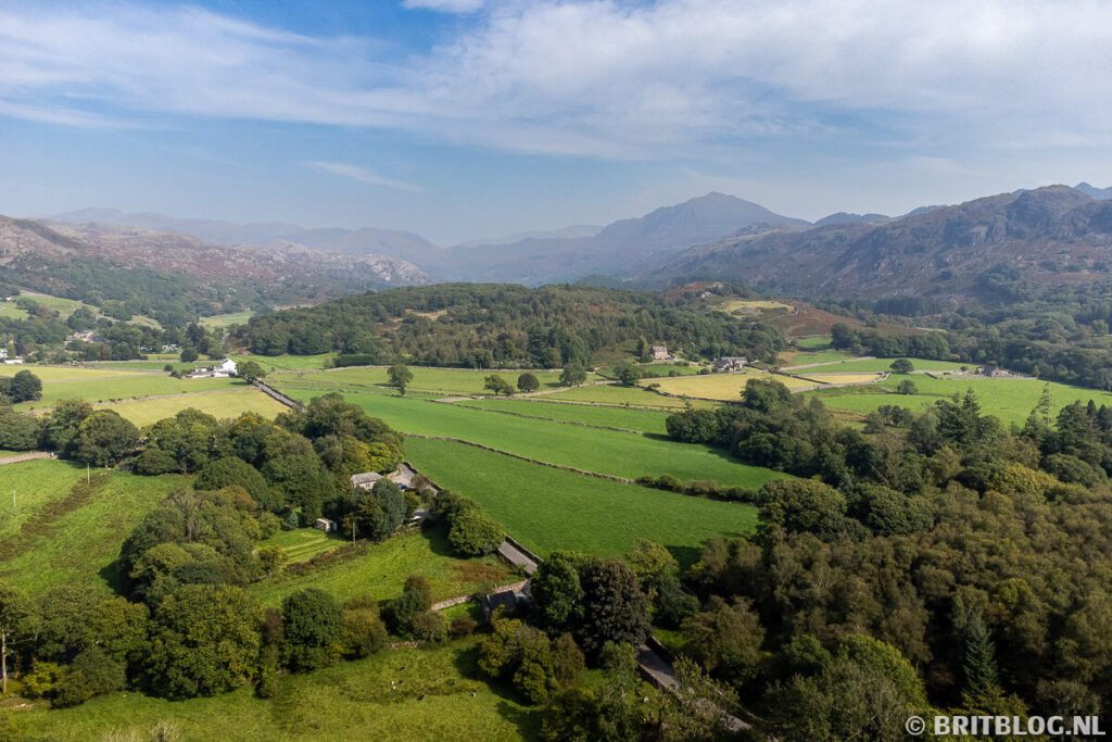 Luchtfoto van de Eskdale-vallei in het Lake District met groene velden, bomen en bergen op de achtergrond onder een blauwe lucht.