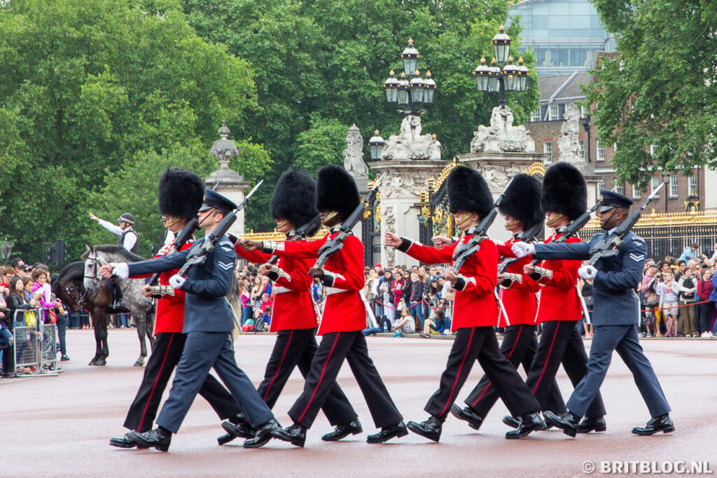 Britse wachters en militairen van de luchtmacht marcheren samen tijdens de wisseling van de wacht bij Buckingham Palace.