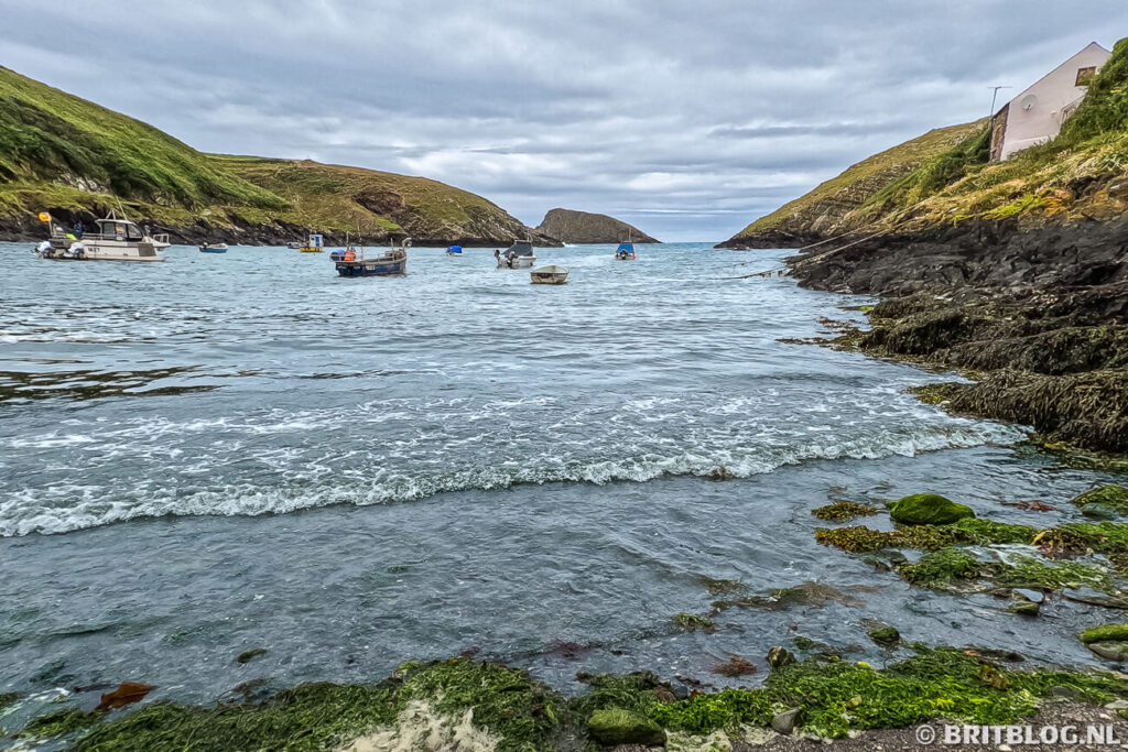 Uitzicht op de natuurlijke haven van Abercastle in Pembrokeshire met vissersbootjes en groene heuvels.