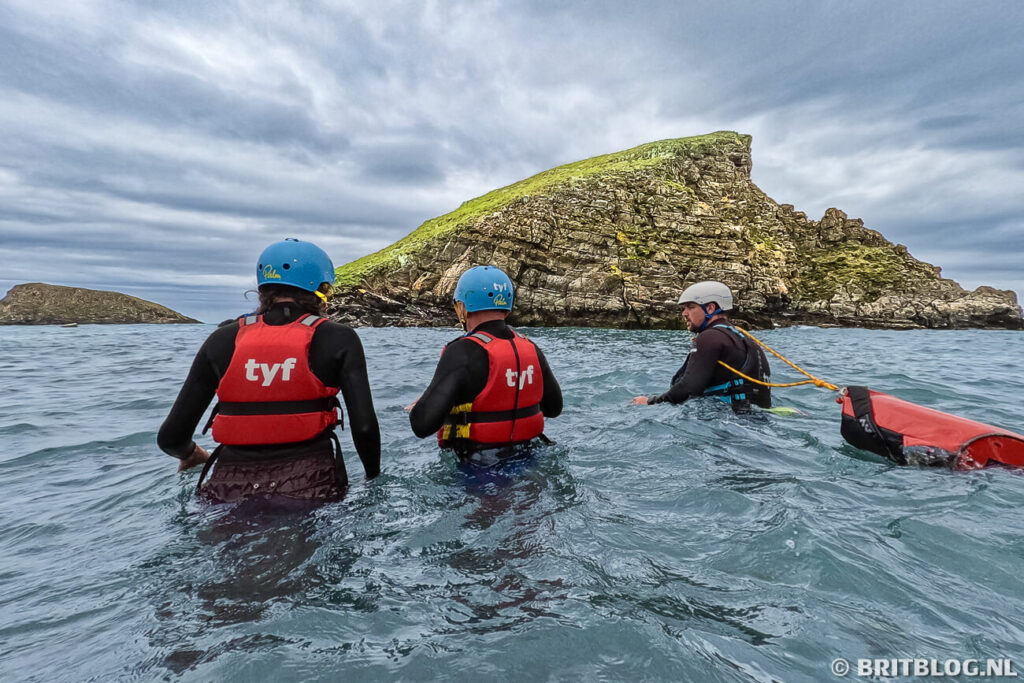 Gids en deelnemers tijdens coasteering bij Abercastle, met het eiland Ynys-y-Castell op de achtergrond.