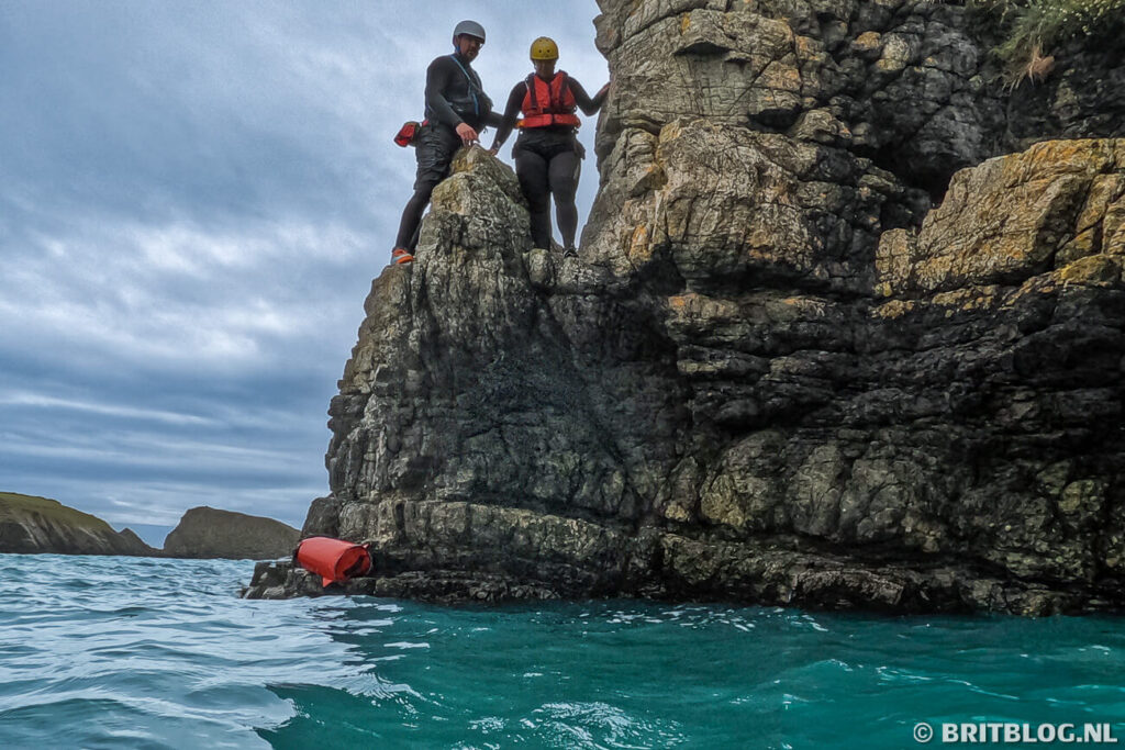 Deelnemers springen van een klif in het water tijdens coasteering in Pembrokeshire, Wales.