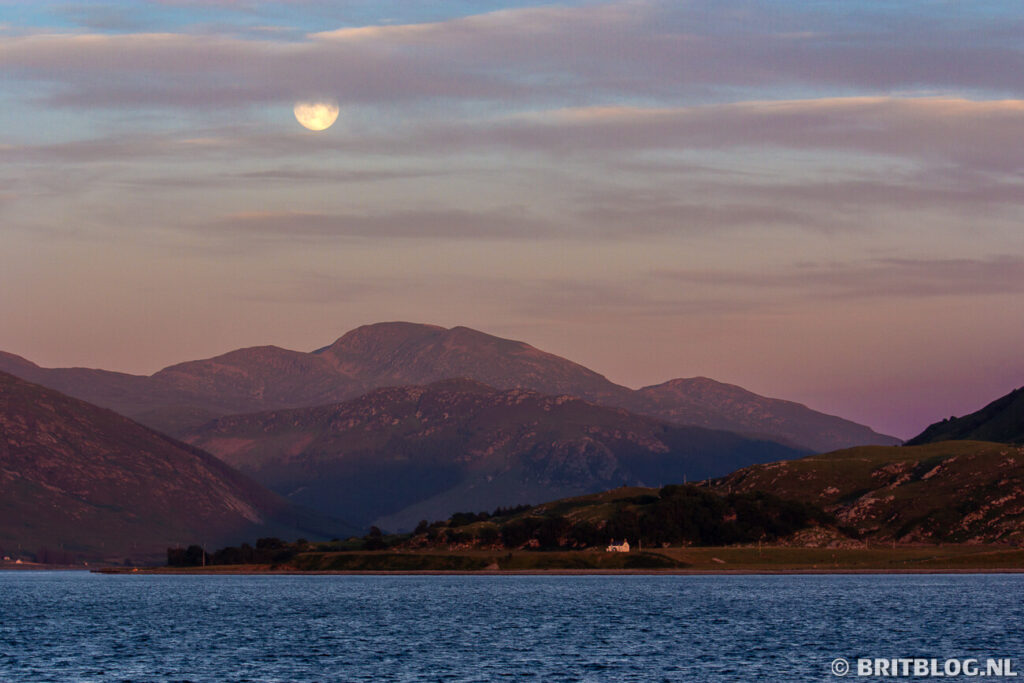 Loch Broom bij Ullapool tijdens zonsondergang met de maan boven de bergen.